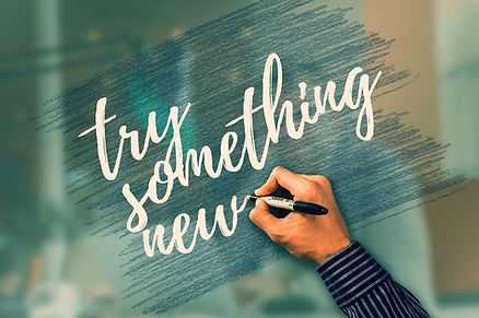 A hand writing the words "try something new," on a board.